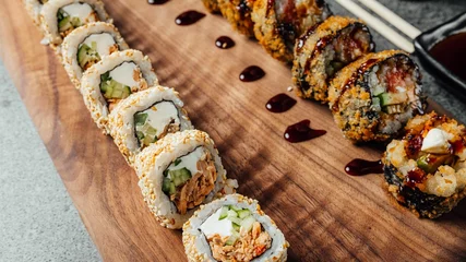 Foto op Aluminium Closeup of a set of delicious fresh sushi rolls, chopsticks, and soy sauce on a  wooden board © Aleksandrs Muiznieks/Wirestock Creators