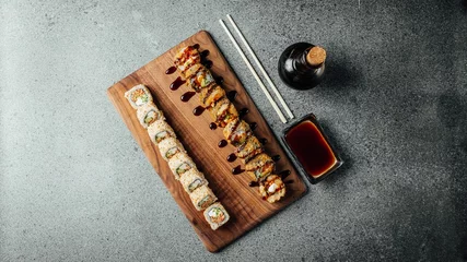 Fotobehang Top view of a set of delicious fresh sushi rolls, chopsticks, and soy sauce on a  wooden board © Aleksandrs Muiznieks/Wirestock Creators