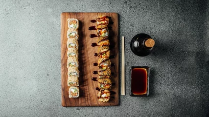 Gordijnen Top view of a set of delicious fresh sushi rolls, chopsticks, and soy sauce on a  wooden board © Aleksandrs Muiznieks/Wirestock Creators