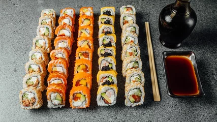 Gordijnen Set of delicious fresh sushi rolls, chopsticks, and soy sauce on a  gray surface © Aleksandrs Muiznieks/Wirestock Creators