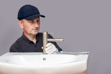 The master plumber screws the faucet to the sink in the bathroom