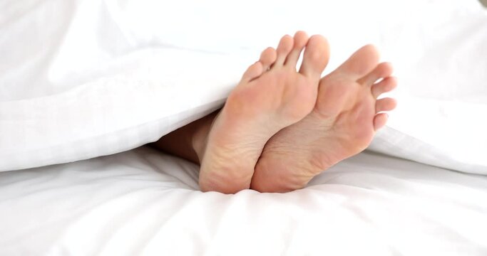 Woman in bed with white linens at home closeup on legs