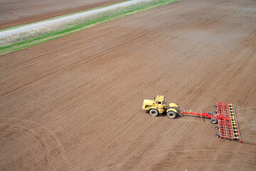 Grain plantations separated by a field road. A tractor with a cultivator is working in the field....
