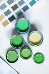 Tiny sample paint cans during house renovation, process of choosing paint for the walls, different green colors, color charts on background