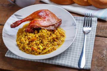 Spelled with vegetables and a duck leg in a light plate next to it on a napkin on the table.