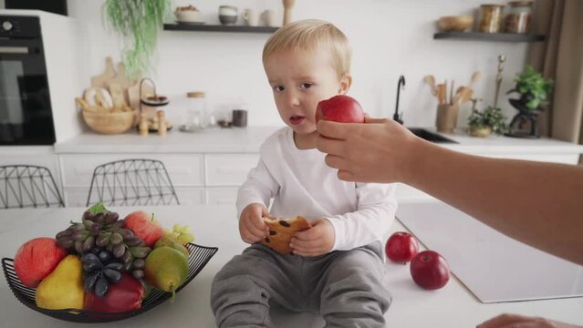 Mom tries to get the child to eat healthy food, but the child pushes her hand away and continues to eat cookies
