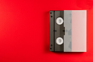 Black vintage VHS videotape cassette in a white case on red background. Plastic retro video...