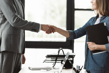 Cropped view of smiling woman with resume shaking hand of businessman during job interview in office.