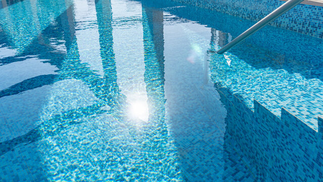 Piscina con reflejos de sol de la ma&ntilde;ana con venecitas azules y turquesas con escalera