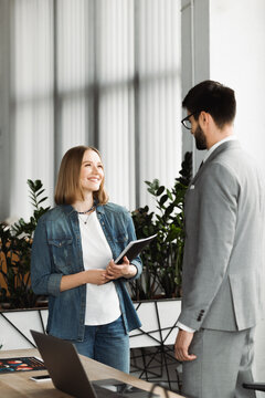 Smiling job seeker holding paper folder near businessman during interview in office.