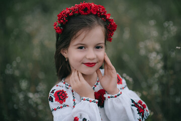 A young girl with very long hair in Ukrainian national dress embroidery and hoop with poppies on outside. Makeup - red lipstick