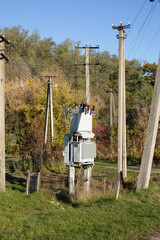 Old small electric transformer outdoors behind the village, wires and a pole.