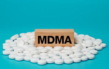 MDMA word on wooden block on pile of white pills on blue background. MDMA Pill known as ecstasy E...
