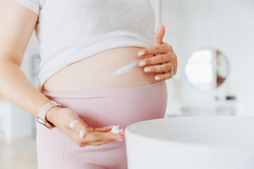Closeup cream in hand of pregnant woman for belly to moisturize skin and improve elasticity to...