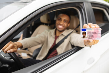  Happy young african man showing his driver's license from open car window