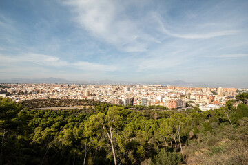 Fototapeta na wymiar Panorámica del paisaje de la ciudad de Alicante con sus edificios y su parque bajo un cielo azul con algunas nubes en el último viaje de trabajo. 
