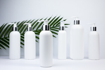 Set of white cosmetic bottles mockup with palm leaf. White plastic bottles with shampoo and conditioner and shower gel on a white background. Mockup cosmetic bottle on white background