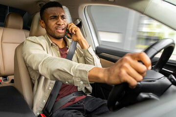 Angry african young man fighting on the phone while driving a car, careless driver using his...
