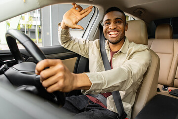 Young african american man smiling while driving a car, waving hello.