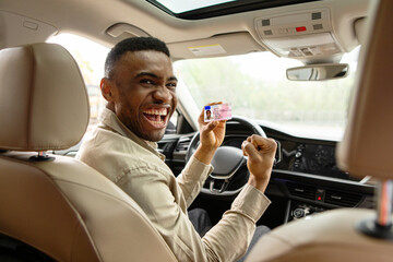  Happy young african man showing his driver's license while driving a car