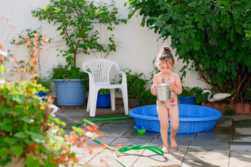 Pretty young girl watering plants with a bucket on a summer day in the backyard