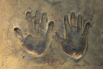 Handprint of a man and a woman on a cement or concrete surface in gold color