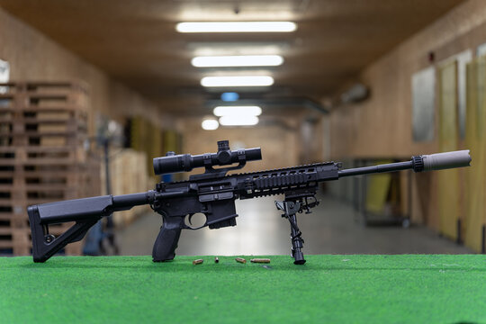 A rifle with an optical sight and a silencer in a shooting range.