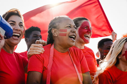 Multiracial red sport football fans celebrating team victory in world championship game at stadium - Soccer supporters having fun in crowd - Focus on African senior woman face