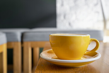 Yellow cup with coffee on a wooden table in a cafe.
