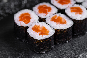 Asian cuisine. Roll with salmon on a black stone on a black background. rice nori salmon