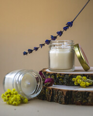 Wax candles in glass jars on wood stand. Set of natural soy wax scented candles withs herbs on beige background.
