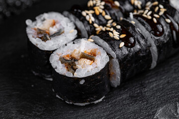 Asian cuisine. Roll with eel on a black stone on a black background. rice nori eel sauce unagi sesame