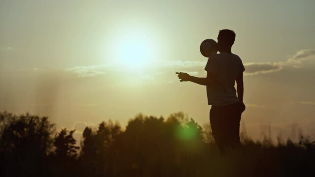 Silhouette of a guy kicking a ball. Playing football at sunset in nature. High quality 4k footage