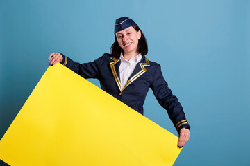 Smiling stewardess holding yellow empty advertising banner with copy space. Happy flight attendant,...