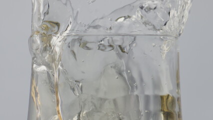 Splashes white wine goblet close up. Ice cube falling in overflowing beverage.