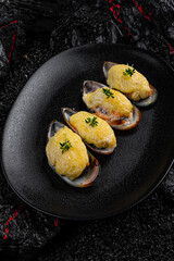 Asian cuisine. Oysters baked with cheese in a black plate on a black background.