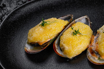 Asian cuisine. Oysters baked with cheese in a black plate on a black background.