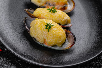 Asian cuisine. Oysters baked with cheese in a black plate on a black background.