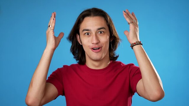 Handsome thinking gender fluid young man 20s, looks at camera gives mind blown gesture showing explosion of ideas posing on blue background.