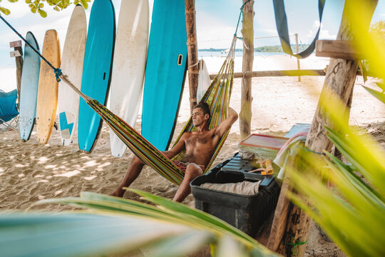 imagen de un hombre acostado en una hamaca en la playa  esperando clientes muy relajado en su negocio de surf