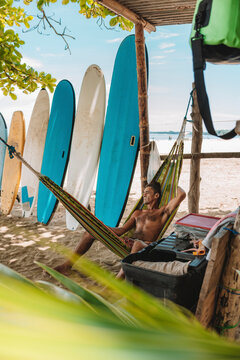 imagen vertical de un hombre acostado en una hamaca en la playa en su negocio de escuela de surf esperando clientes muy relajado