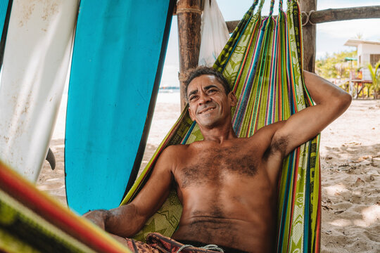 Retrato de un hombre sin camisa y con rizos muy sonriente acostado en una hamaca en una playa del caribe de Costa Rica 