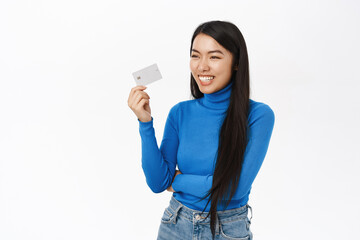 Bank and shopping. Smiling asian girl shows credit card, looks happy, concept of buying contactless, stands over white background