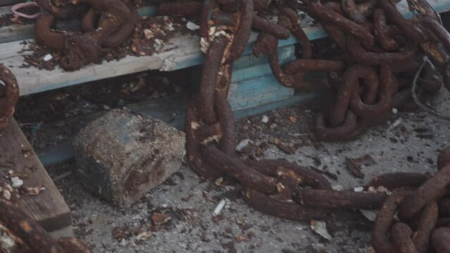 an old metal chain covered with rust from moisture lies on the seashore. A large chain covered with corrosion lies in a pile of garbage.