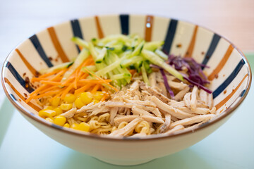 angle view bowl of cold noodles with shredded chicken and cucumber and carrot and purple cabbage