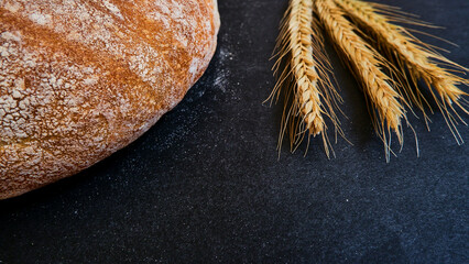 Ears and bread covering quarter of the area on black background, selective focus and isolated photo.