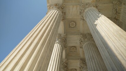 Looking up at the top of Corinthian columns in front of US Supreme Court in Washington, DC, showing power over people and business.