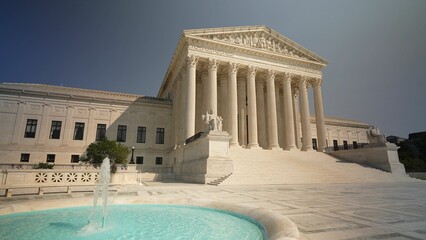 Facade of US Supreme Court building with Authority of Justice sculpture in front in Washington DC on a sunny summer evening.