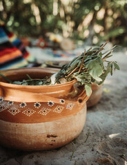 Aromatic herbs macerating in ceramic pot in exotic white sand garden with tropical forest in the blurry background during sacred indigenous ceremony in Tulum