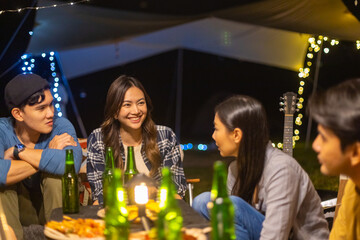 Group of Happy Asian people enjoy and fun outdoor lifestyle camping together on holiday travel vacation. Man and woman friends playing guitar and singing together while having dinner at summer night.